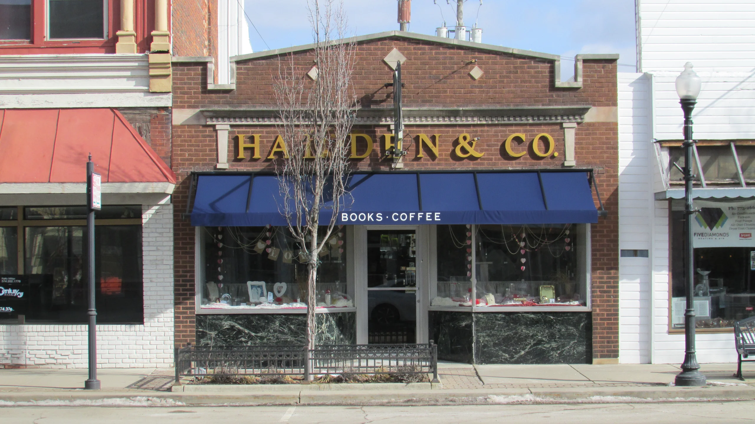 Brick bookstore storefront with a navy awning labeled BOOKS · COFFEE and books displayed in the windows.